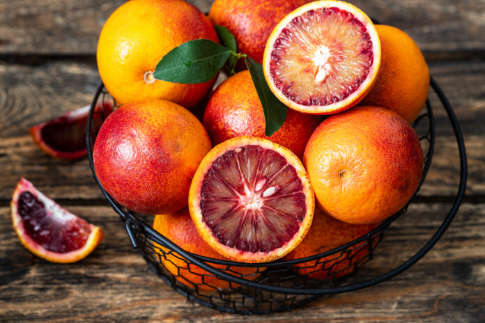 Blood oranges in a metal basket on a wood background.